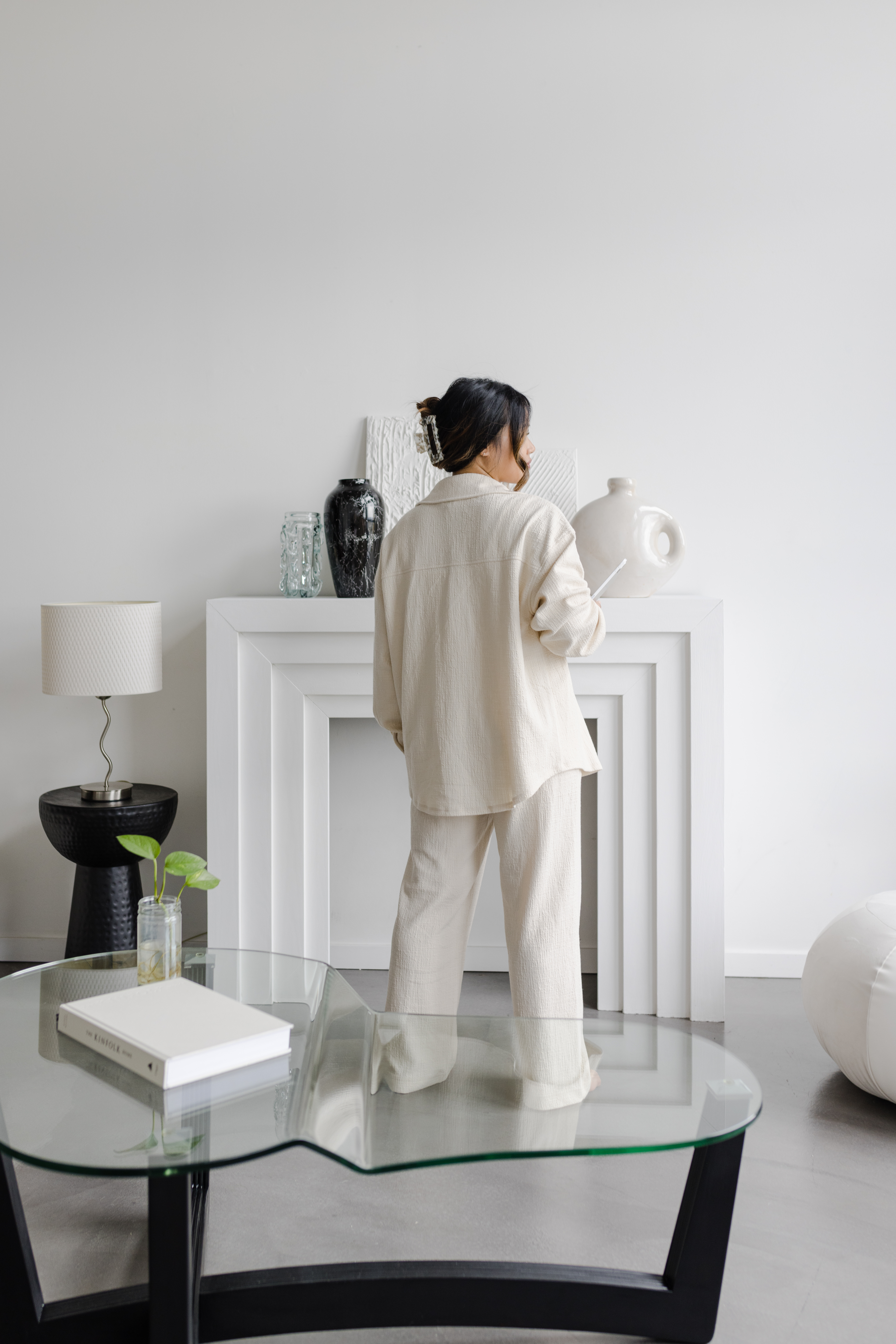 Woman in off-white linen outfit standing inside a stylish, modern white photography studio and around home decor.